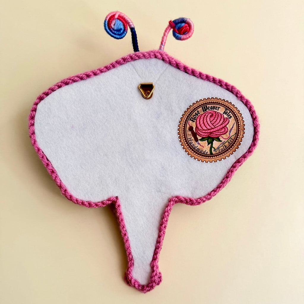 Back View of the handmade punch needle textile dragonfly, showing a meat soft felt backing, a Rose Weaver tales brand label, and a segure metal hanging loop.