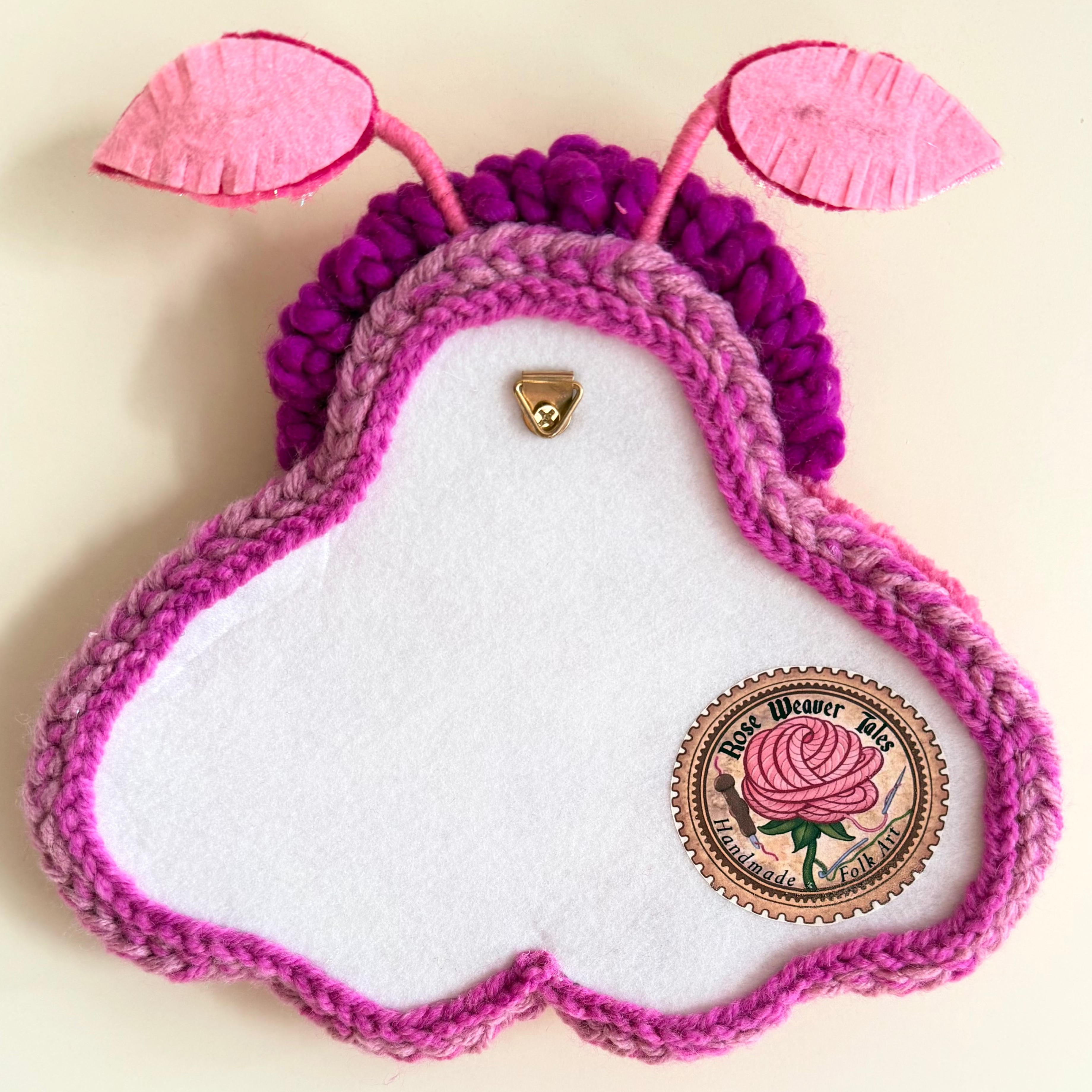 Back View of the handmade punch needle textile Moth, showing a meat soft felt backing, a Rose Weaver tales brand label, and a segure metal hanging loop.